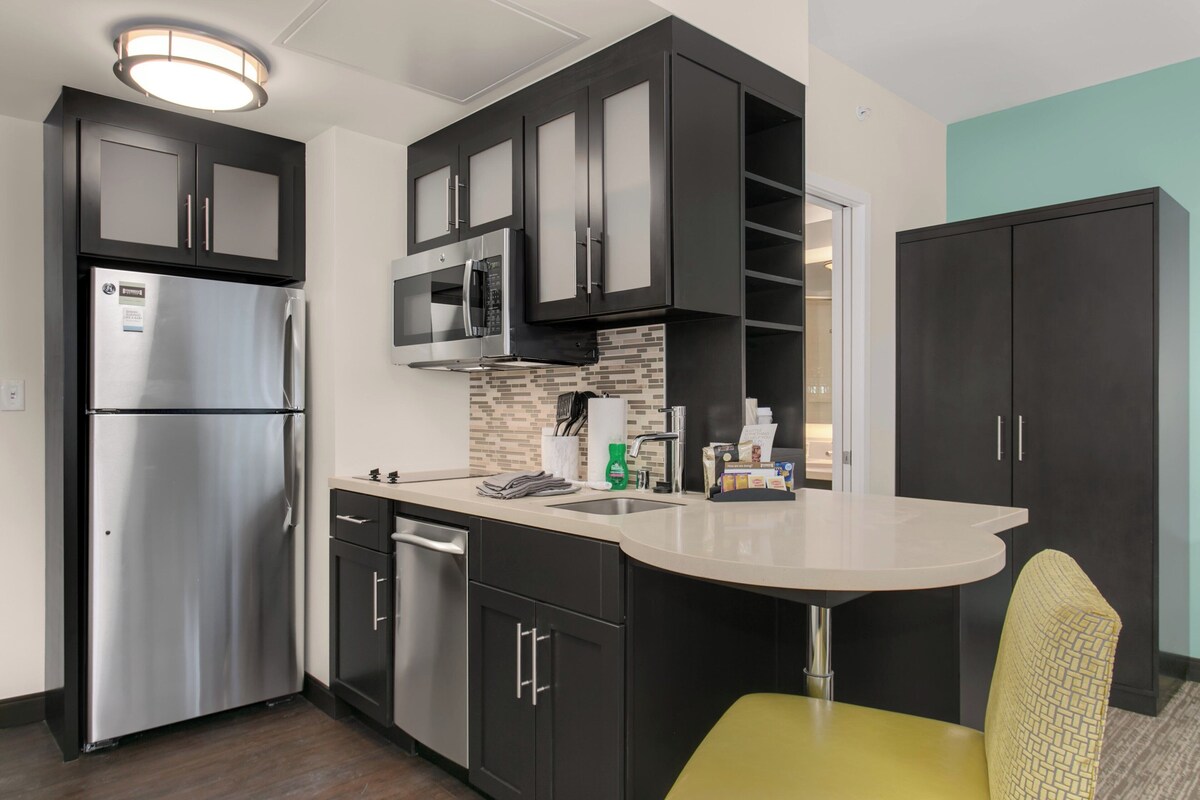 Une cuisine moderne avec des meubles de couleur sombre, des appareils électroménagers en acier inoxydable et un îlot central.