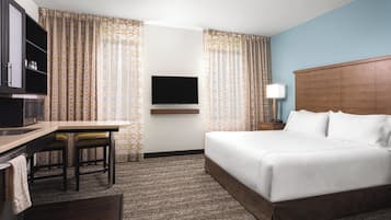 Quarto de hotel com cama, escrivaninha, televisão e luminária.