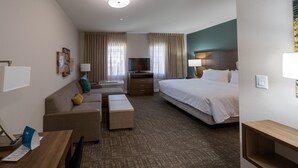 Una habitación de hotel con cama, sofá, escritorio, televisor y ventana con cortinas.