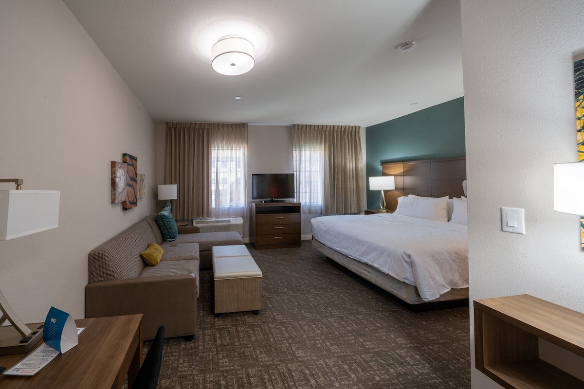 A hotel room with a bed, a sofa, a desk, a TV, and a window with curtains.