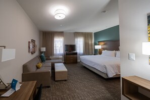 A hotel room with a bed, a sofa, a desk, a TV, and a window with curtains. - Staybridge Suites Houston East - Baytown by IHG (Baytown)