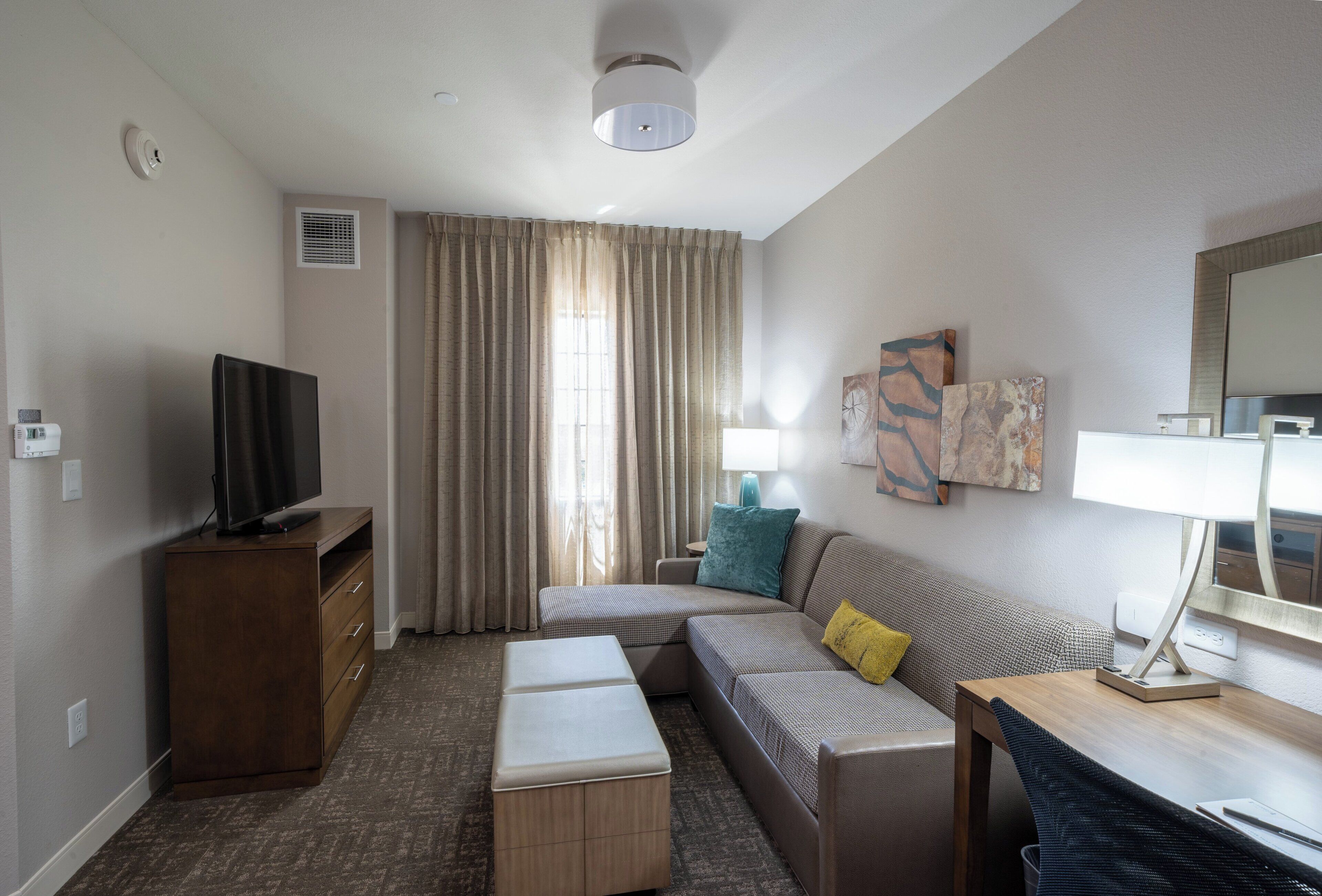 Ein modernes Hotelzimmer mit Fernseher, einer Couch, einem kleinen Tisch und einer Lampe.