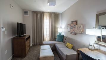 Ein modernes Hotelzimmer mit Fernseher, einer Couch, einem kleinen Tisch und einer Lampe.