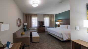 A hotel room with a bed, a sofa, a TV, a desk, and a window with curtains.