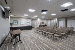 Un salón de conferencias con una larga mesa, sillas, un mostrador de recepción, obras de arte enmarcadas y piso alfombrado.