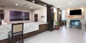 A reception area with a marble counter, a seating area with a chair, a fireplace, and a television mounted on the wall.