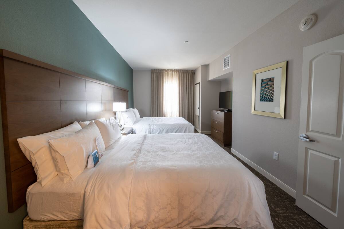 A hotel room with two beds, a wooden headboard, a television, a framed artwork, and a door.