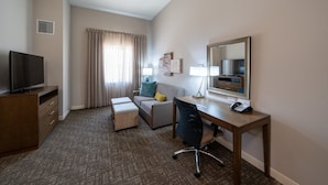 Ein Hotelzimmer mit Flachbildfernseher, Schreibtisch mit Lampe, Stuhl, Sofa mit Kissen und einem großen Spiegel.