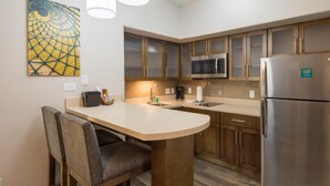 Cocina compacta con microondas, refrigerador y una pequeña isla con asientos.