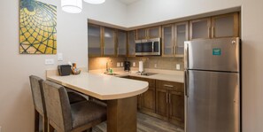 A compact kitchen with a microwave, refrigerator, and a small island with seating. - Staybridge Suites Houston East - Baytown by IHG (Baytown)