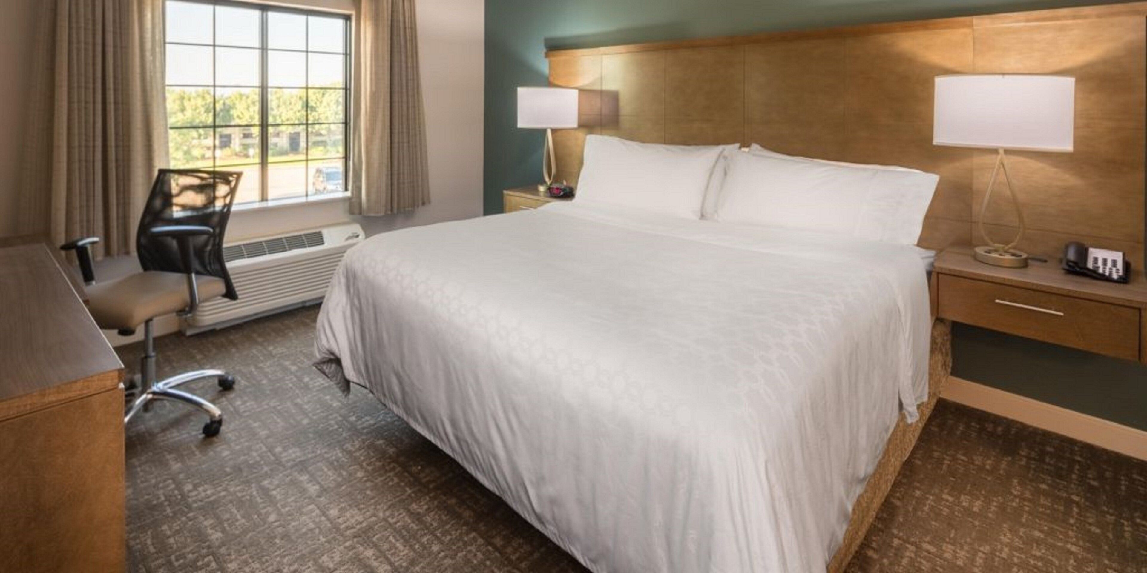 A hotel room with a large bed, two bedside lamps, a desk with a telephone, and a chair.