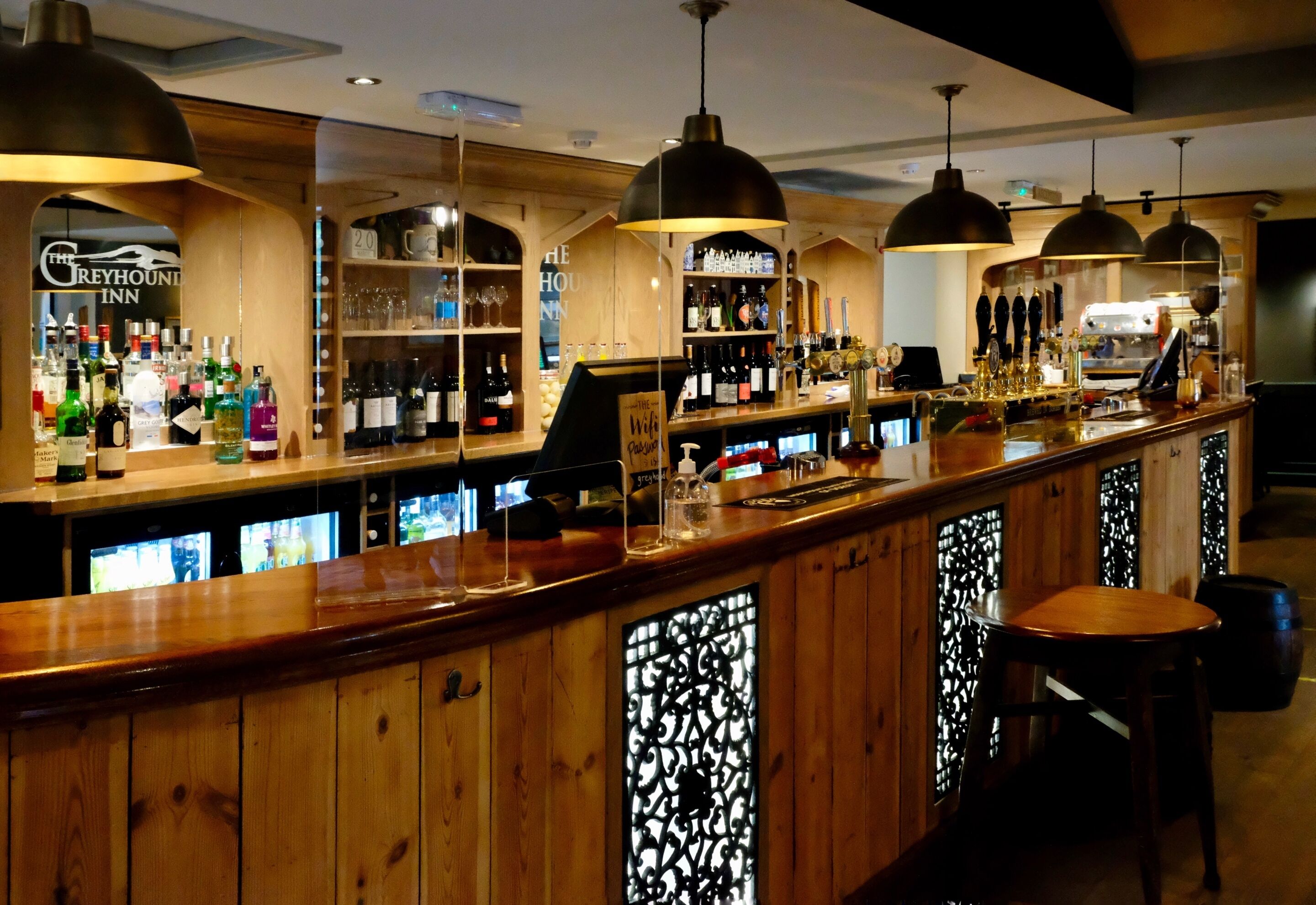 Uma área de bar com painéis de madeira, luminárias pendentes e prateleiras cheias de garrafas e copos.