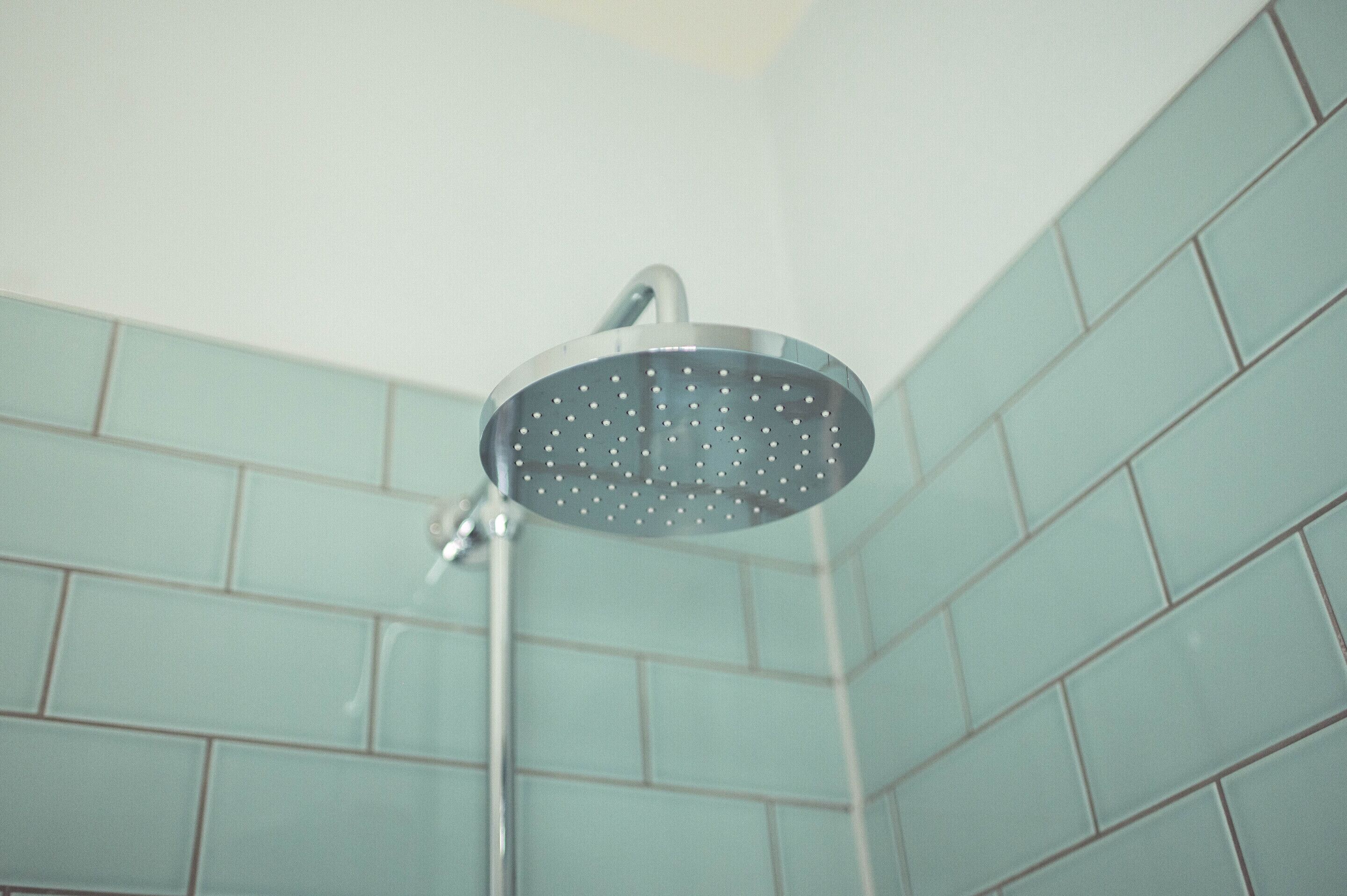 A showerhead in a bathroom with light blue tiled walls.