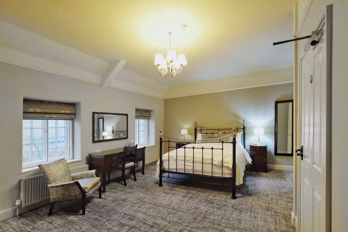 A bedroom with a four-poster bed, a desk, a chair, and a large mirror.