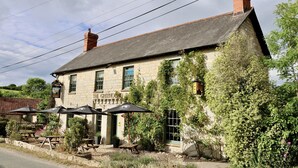 A stone building with a sign reading "The Greyhound Inn." There are outdoor tables and umbrellas, and the building is surrounded by greenery. - The Greyhound Inn Taunton (Taunton)