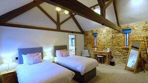 A bedroom with two beds, a desk, a chair, and a stone wall. - The Greyhound Inn Taunton (Taunton)