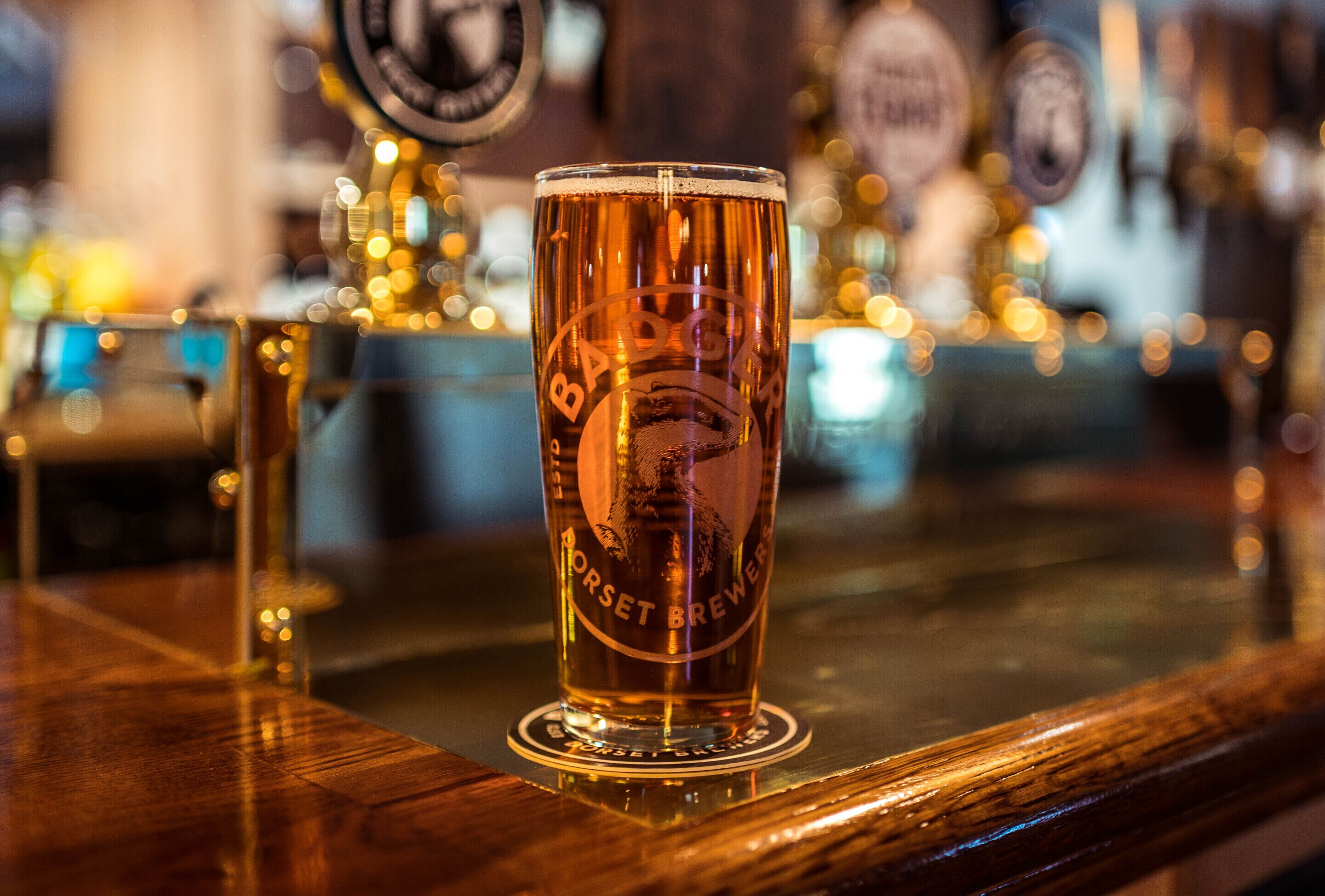 A glass of beer on a bar counter with a blurred background of bar equipment.