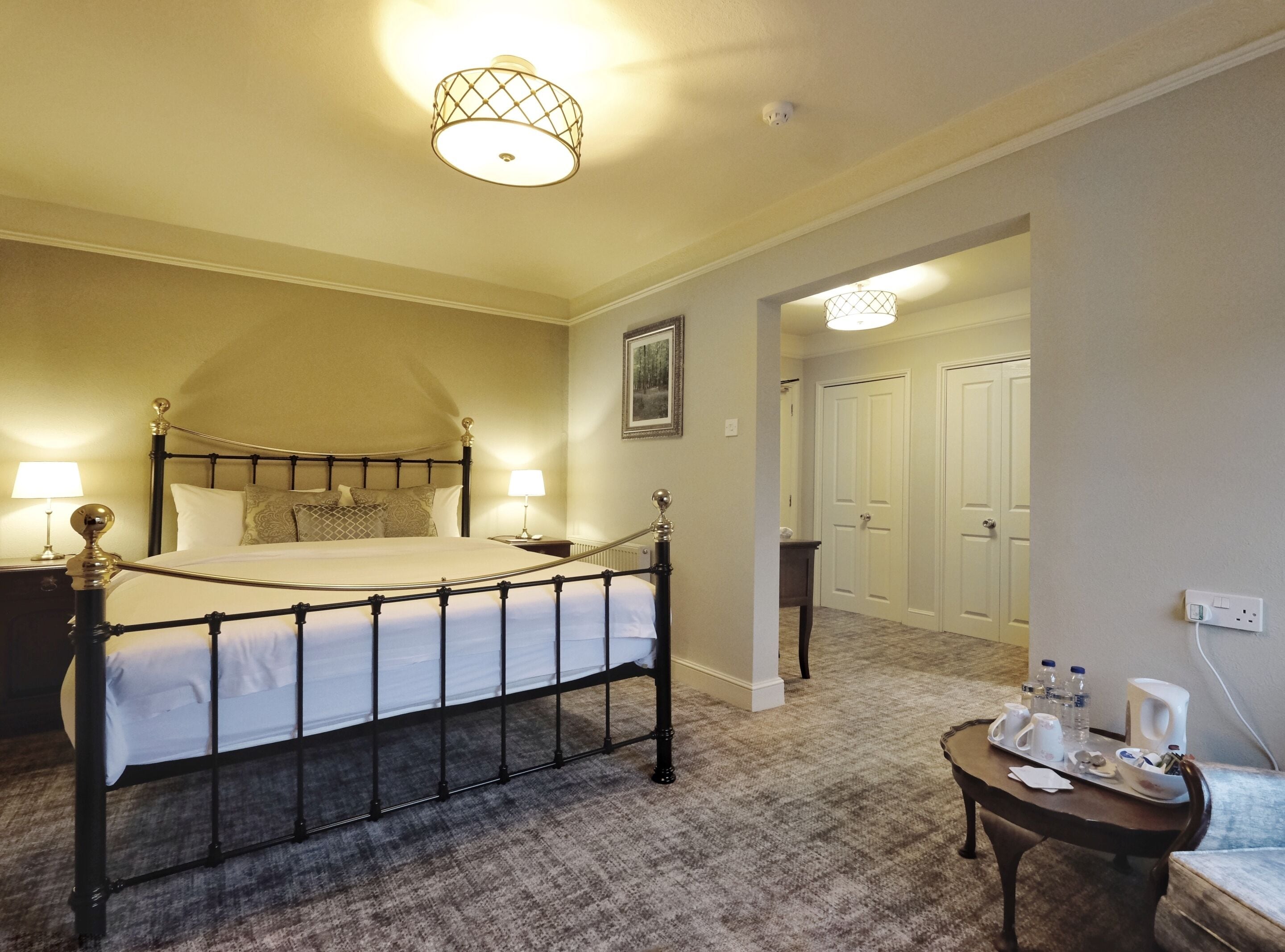 A hotel room with a large bed, bedside lamps, a small table with toiletries, and a hallway leading to a door.