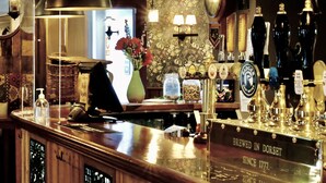 A bar with a wooden counter, a clock, and various bottles and glasses. - The Greyhound Inn Taunton (Taunton)