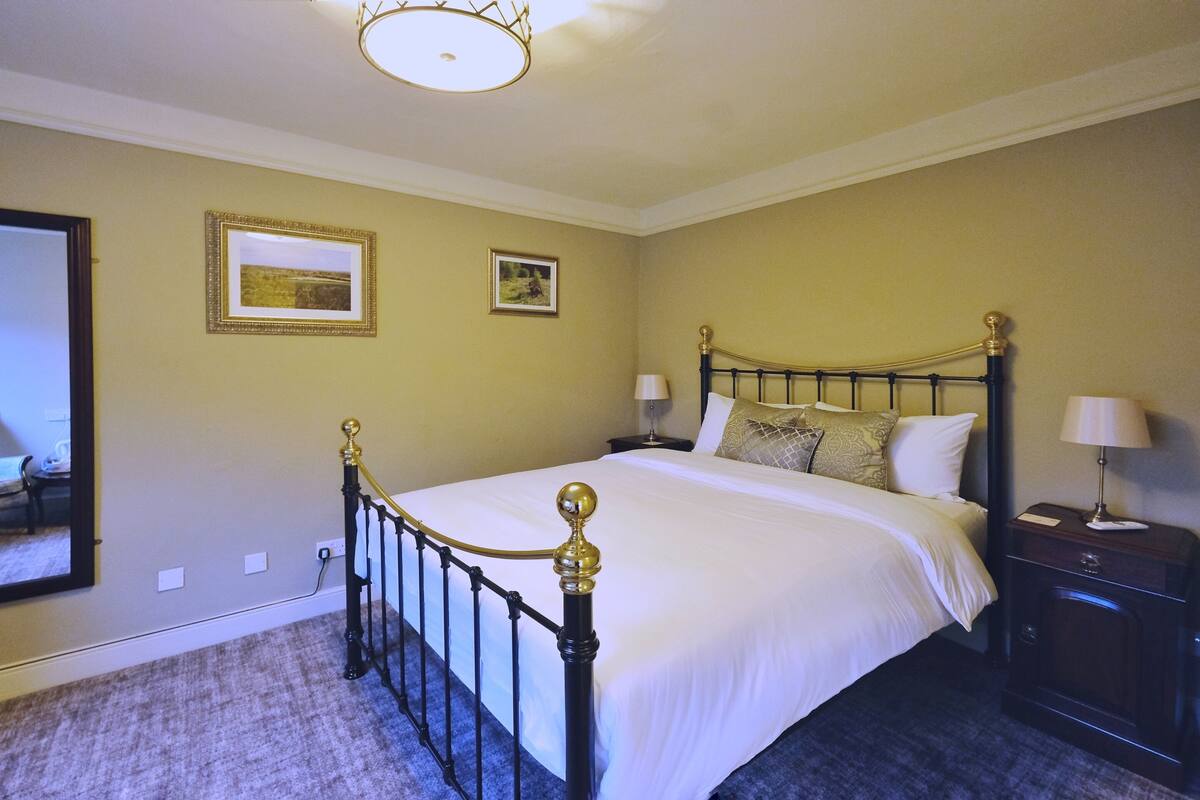 A neatly made bed with a black metal frame and gold accents, a nightstand with a lamp, and two framed pictures on the wall.