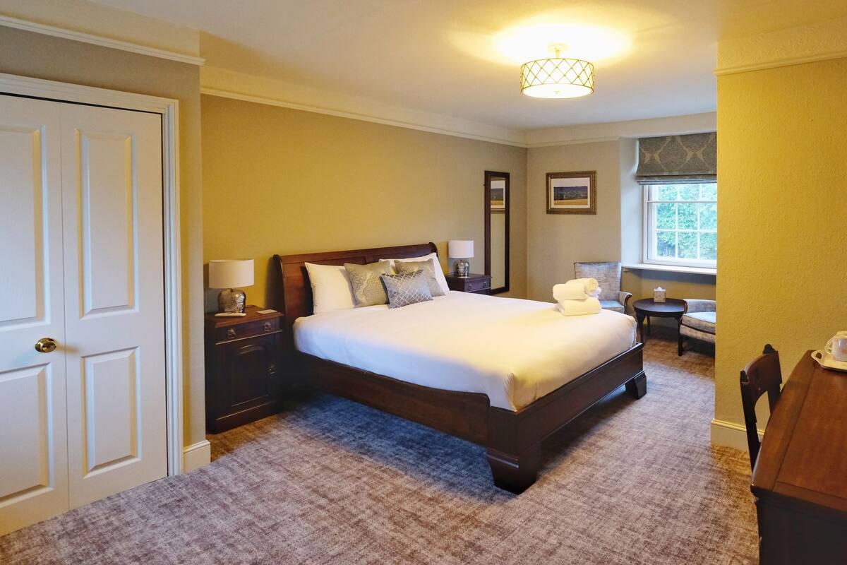 A bedroom with a large bed, a nightstand, a lamp, a chair, and a window.