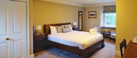 A bedroom with a large bed, a nightstand, a lamp, a chair, and a window.