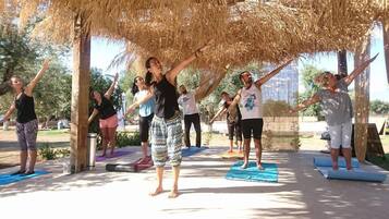 A group of people practicing yoga outdoors under a thatched roof structure.