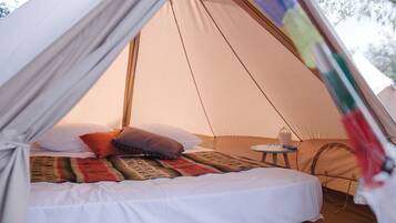 A tent with a bed, pillows, a blanket, and a small table with a lantern.