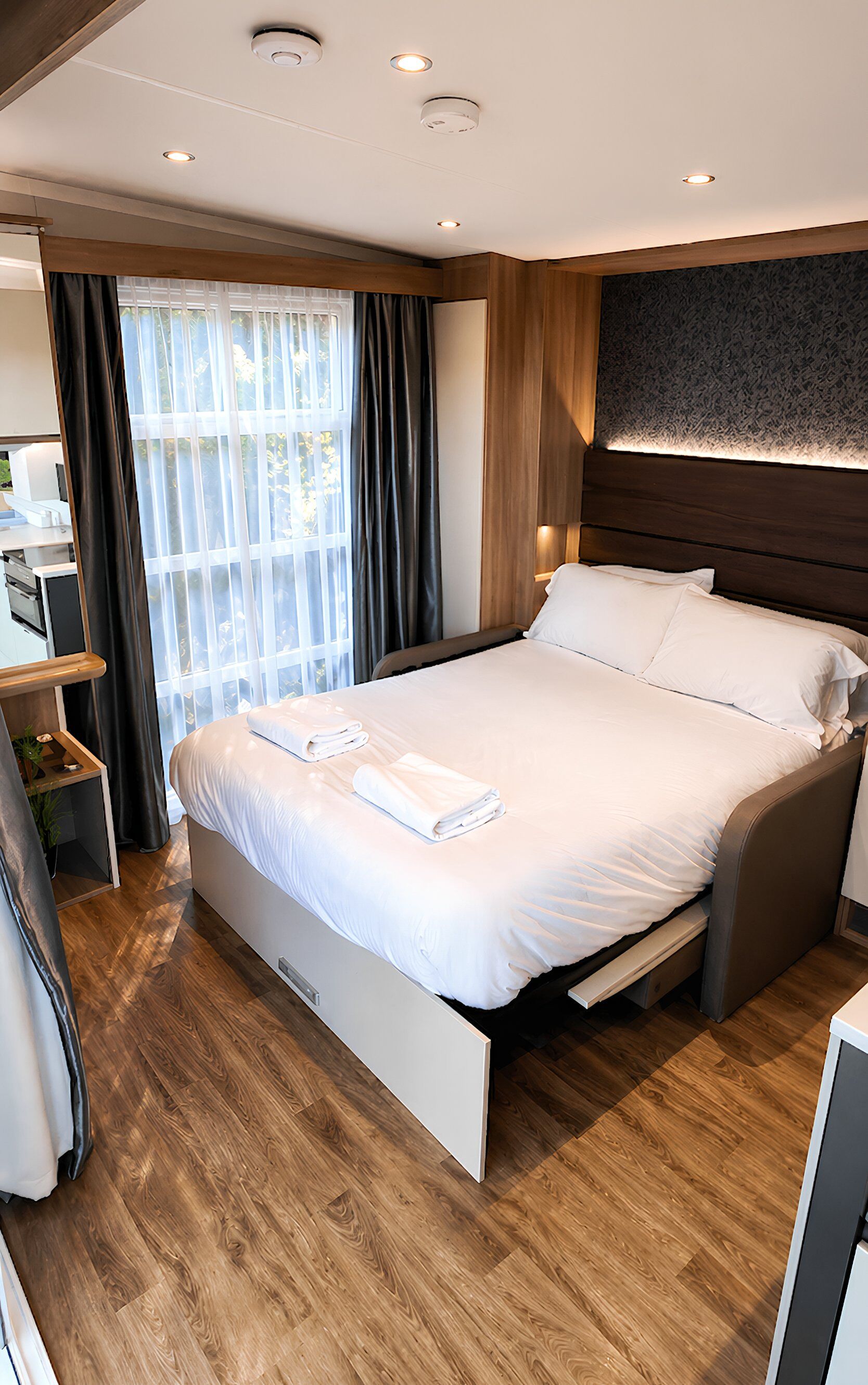 A modern hotel room with a large bed, a desk with a computer, and a window with curtains.