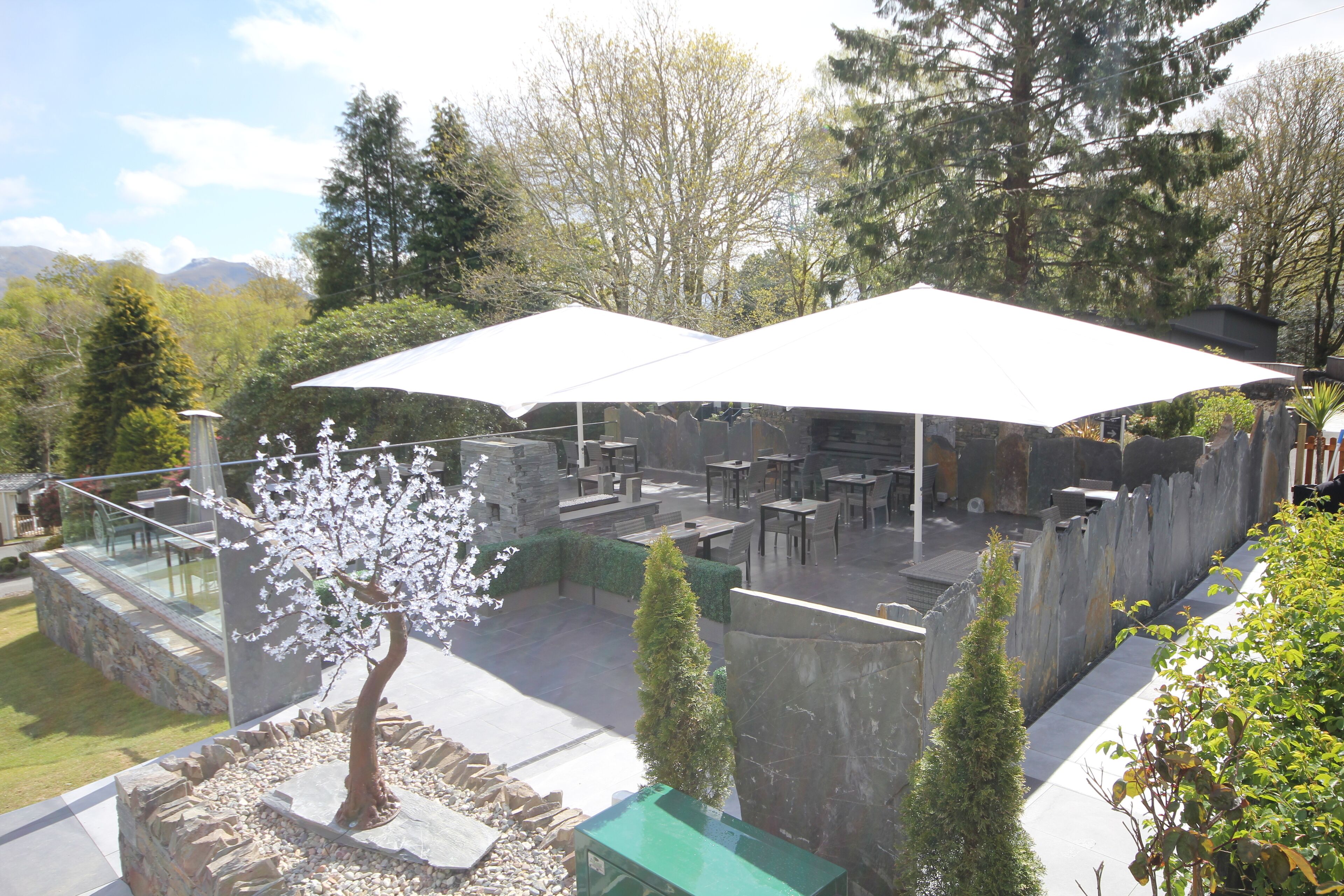 Un espace extérieur aménagé en terrasse, avec des sièges et des tables en pierre, entouré de verdure et offrant une vue sur les montagnes.