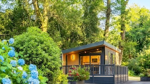 A modern cabin with a deck, surrounded by lush greenery and trees. - Aberdunant Caravans Direct (Porthmadog)