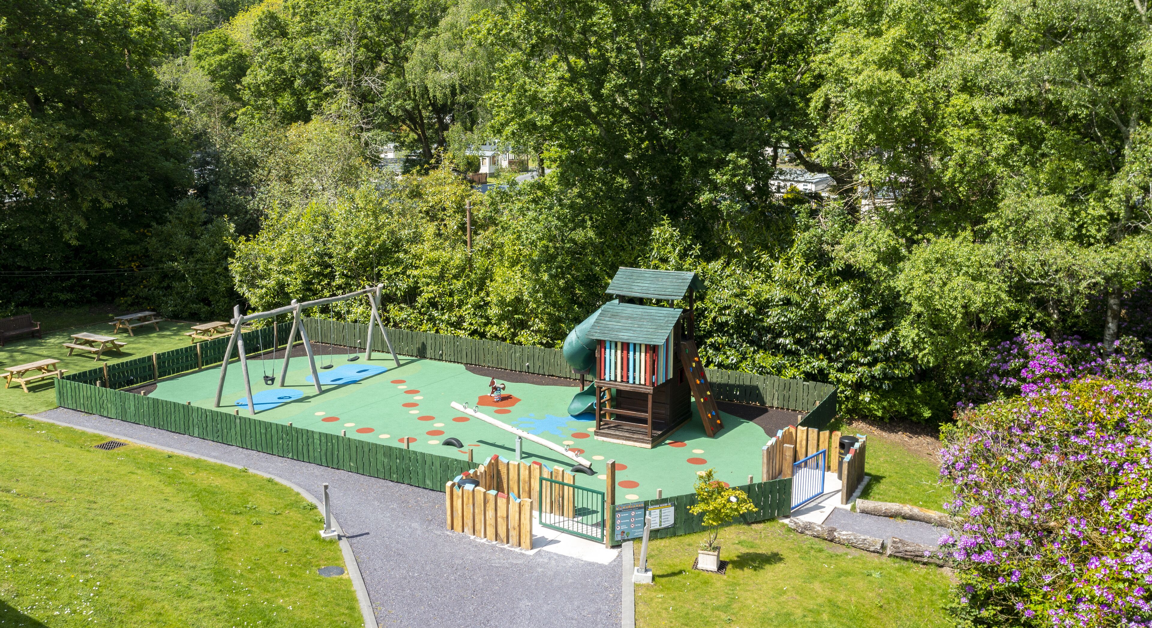 A playground with a slide, swing set, and climbing area surrounded by trees.