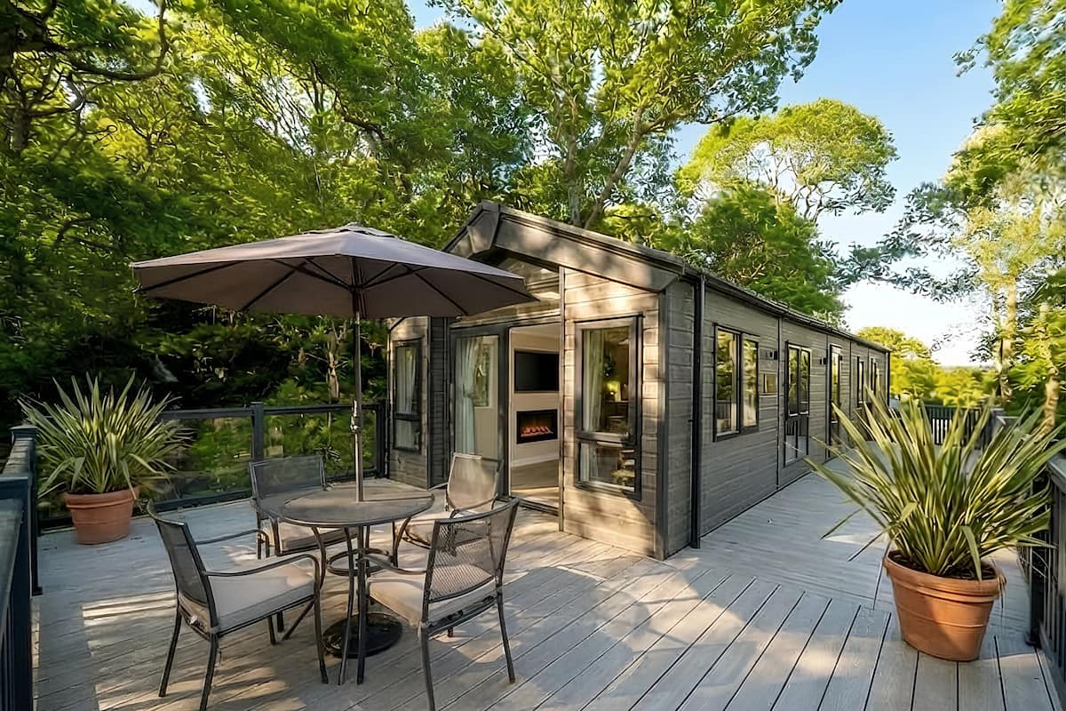 A modern outdoor deck with a dining table and chairs, surrounded by potted plants.