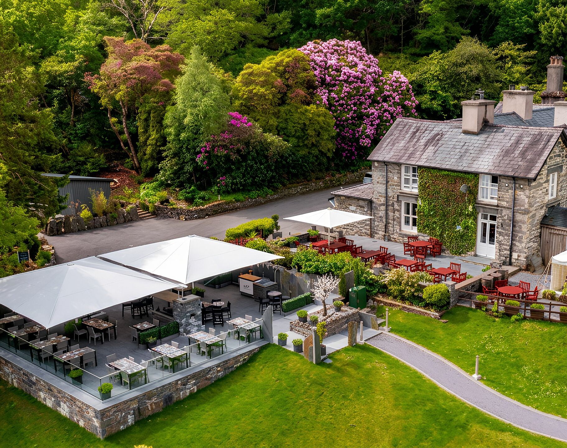 A large outdoor dining area with multiple tables and chairs, a covered seating area, and a stone building with a garden.