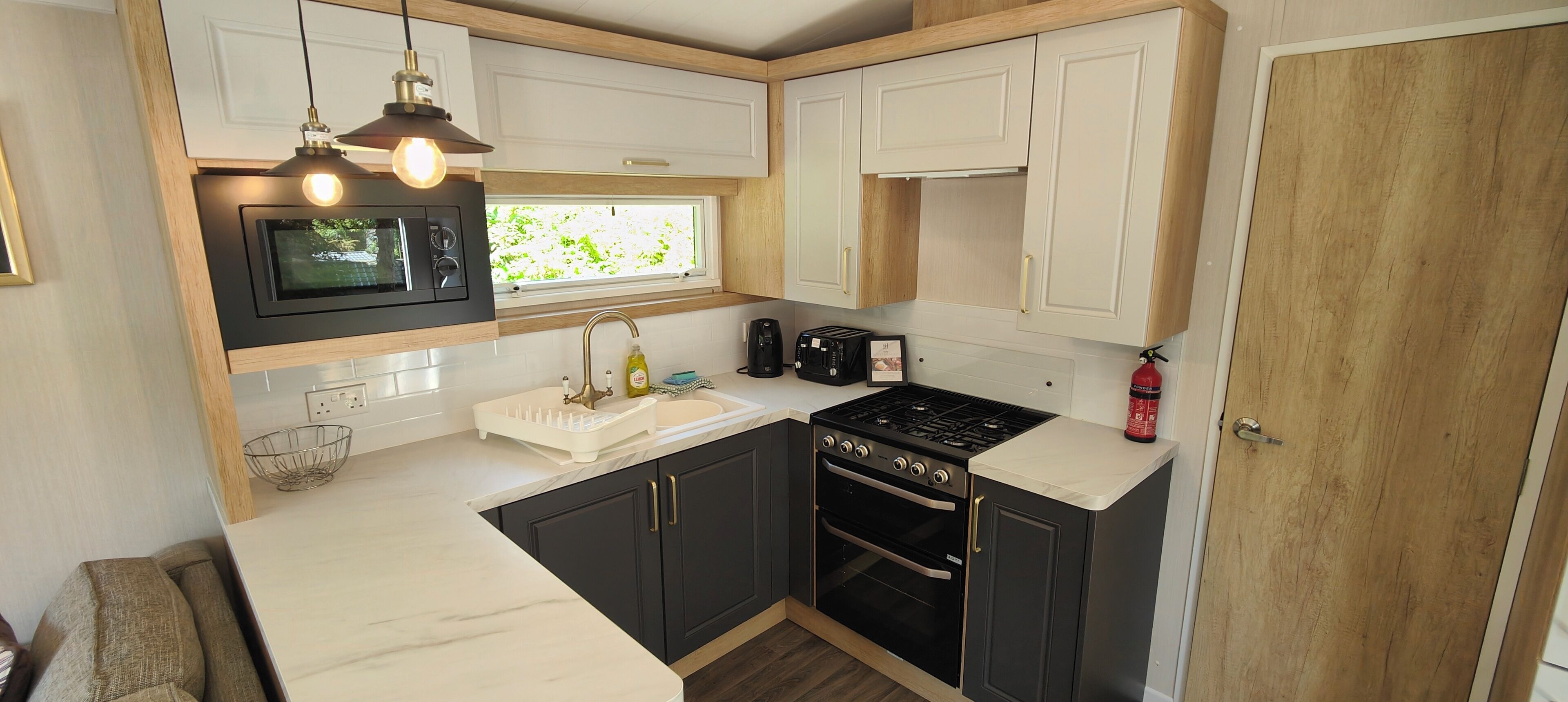 A compact kitchen with a microwave, stove, sink, and wooden cabinets.