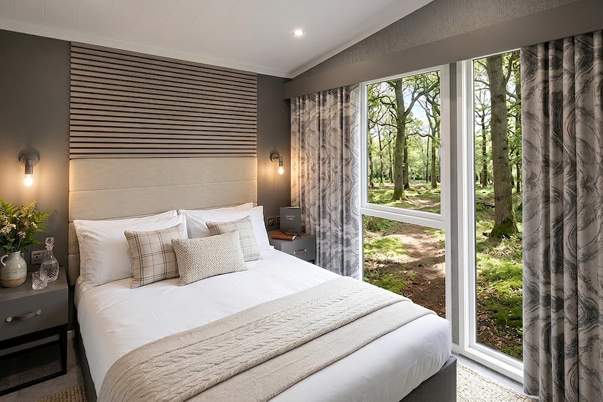 A bedroom with a large bed, bedside tables, a nightstand, a wall-mounted light, and a window with curtains.