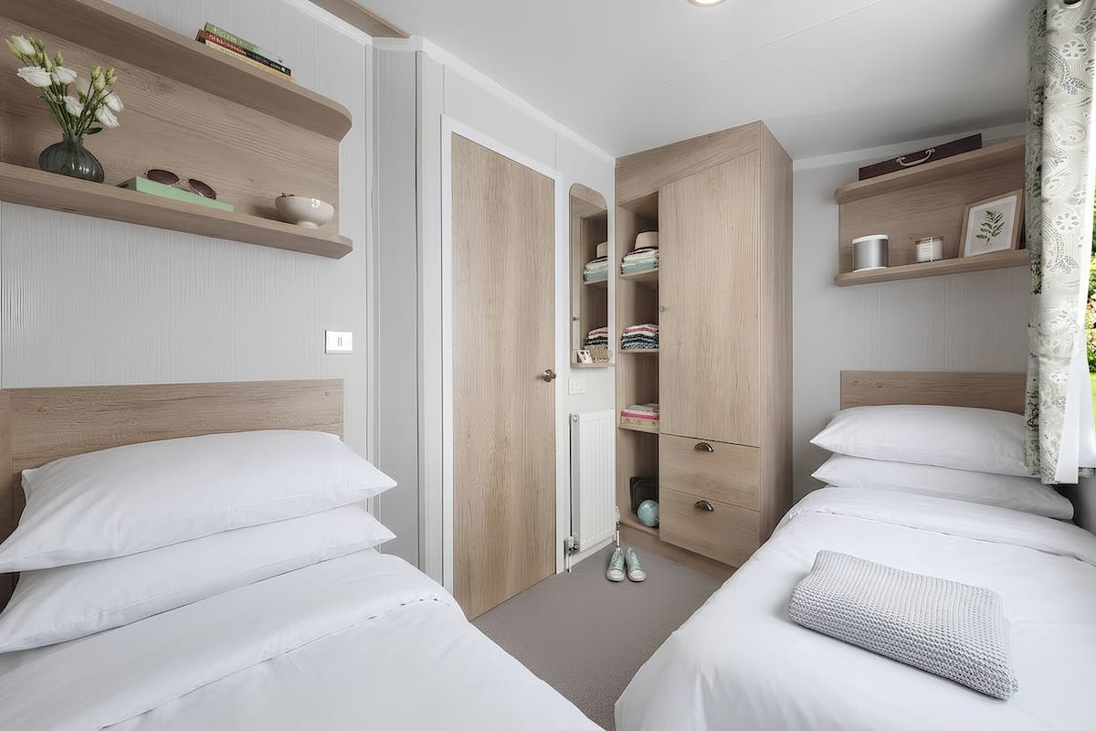 A bedroom with two beds, wooden headboards, built-in wardrobes, and shelves with personal items.