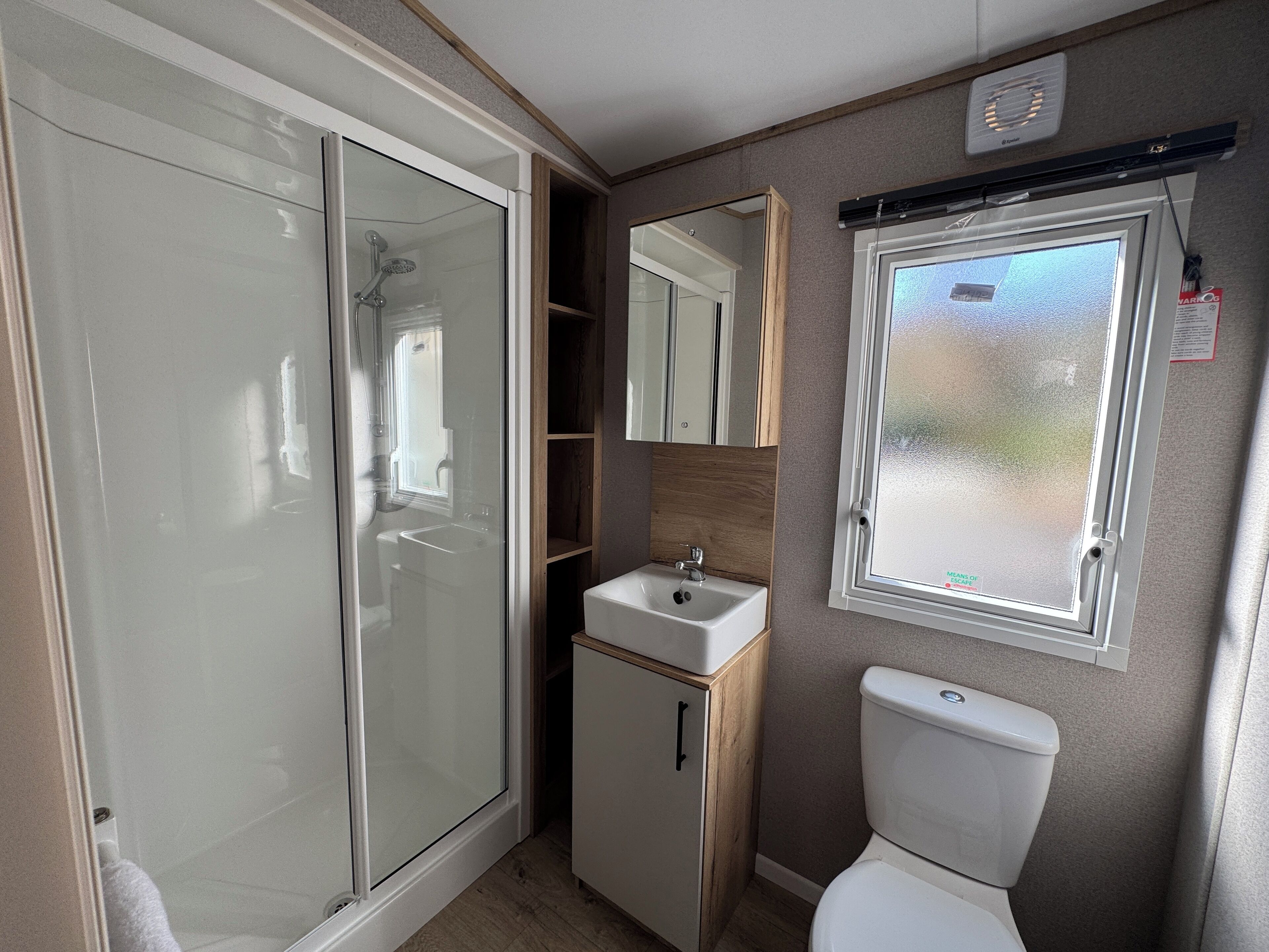 A compact bathroom with a glass shower enclosure, a small sink, and a toilet.