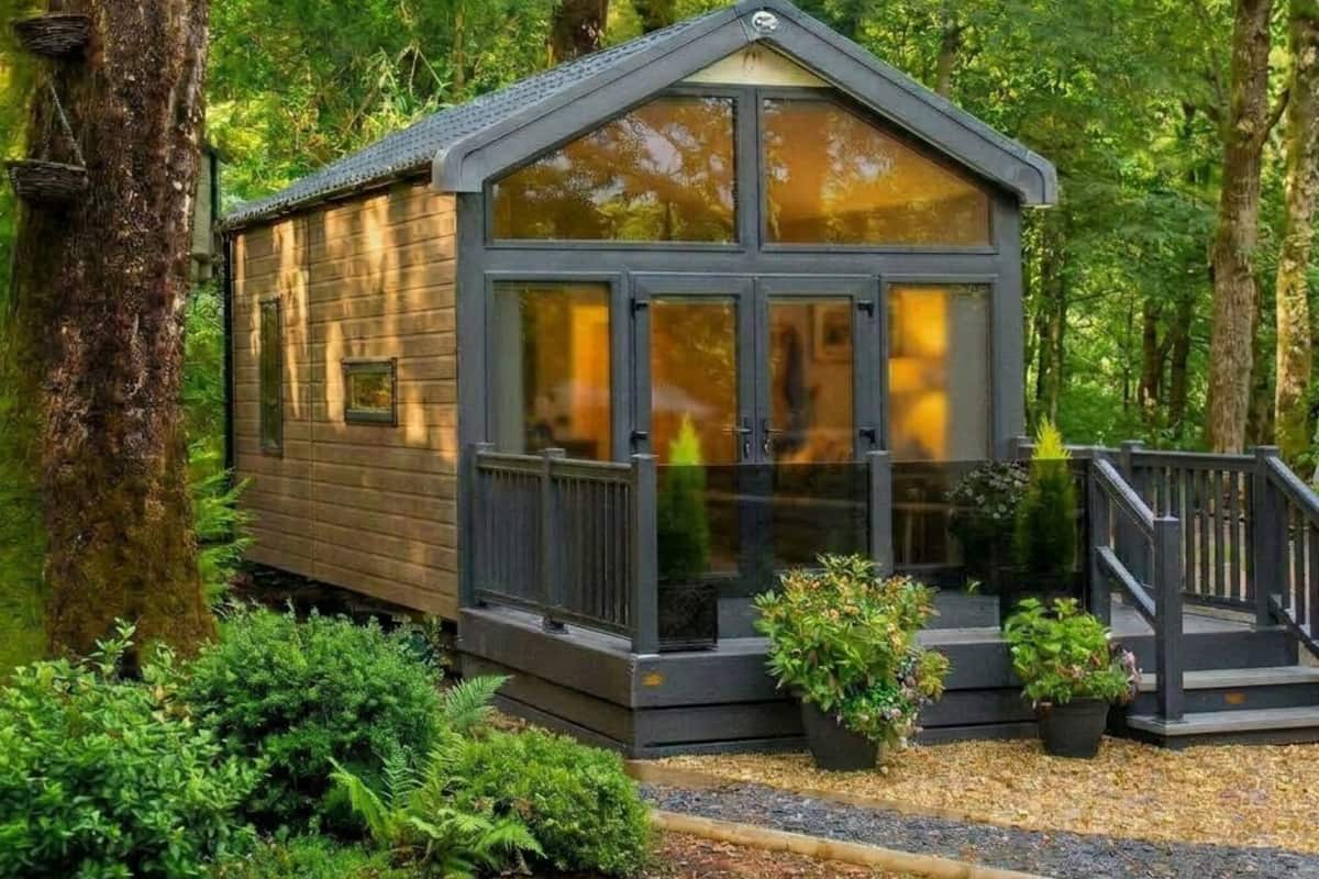 A small, wooden cabin with a porch, surrounded by dense forest.