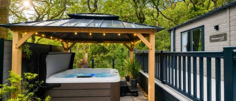 A hot tub under a wooden pergola with string lights, surrounded by potted plants and a deck.