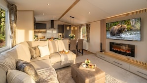 A modern living room with a sofa, a coffee table, a fireplace, and a TV displaying a bear. - Aberdunant Caravans Direct (Porthmadog)
