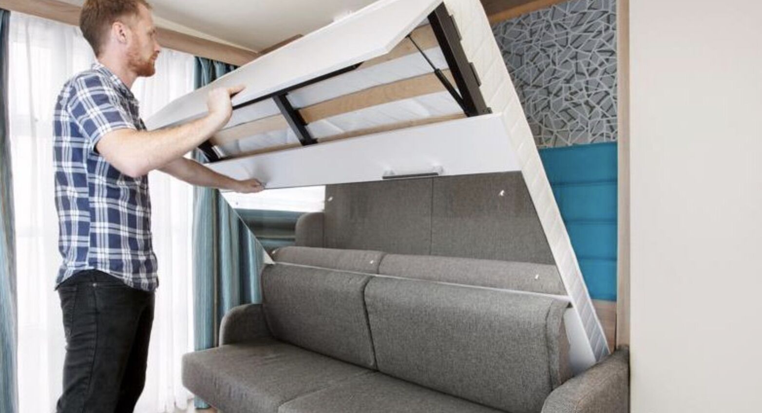 Una persona instalando un sofá cama en una habitación con un papel tapiz estampado y una ventana con cortinas.