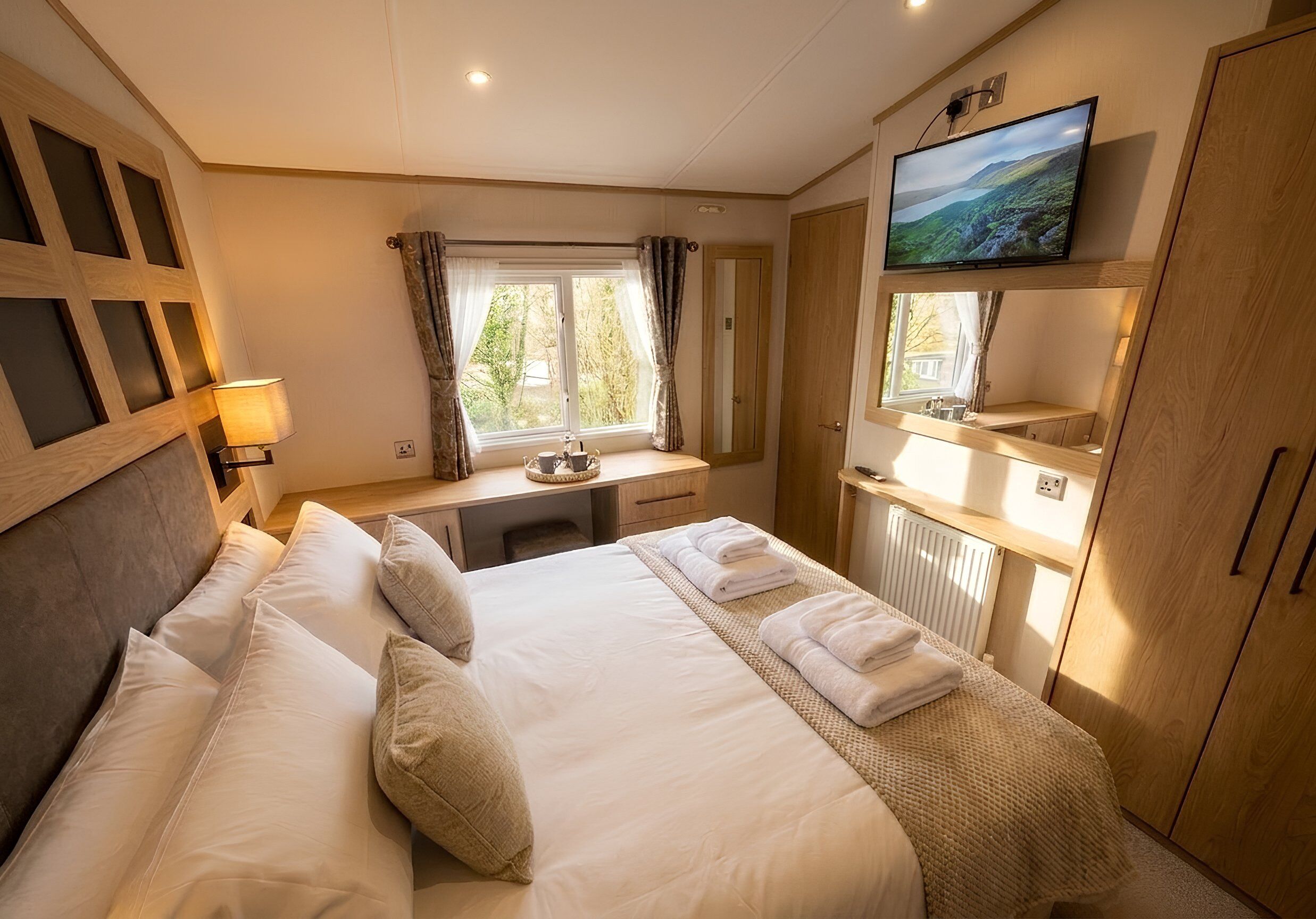 Una habitación de hotel con cama, escritorio, televisor y ventana con cortinas.