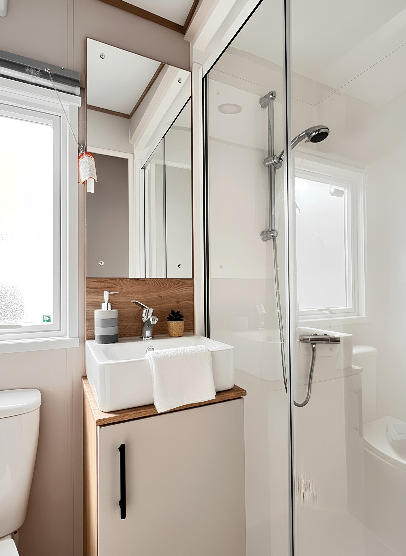 A modern bathroom with a glass shower enclosure, a white sink with a wooden countertop, and a mirror above the sink.