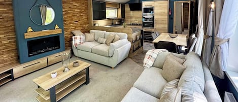 A modern living room with a sofa, coffee table, and a TV. There is a kitchen area with a dining table and chairs.