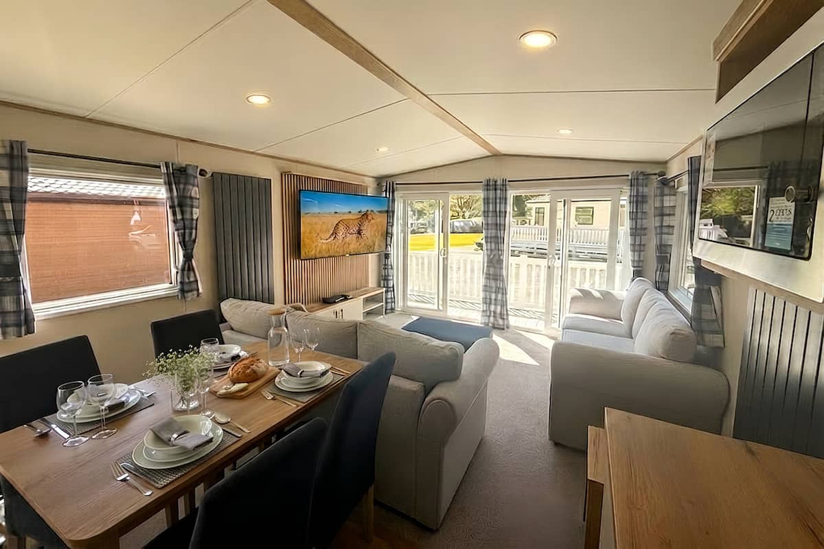 A caravan interior with a dining area, seating, a TV, and a view through the doors.
