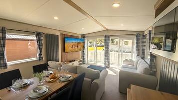 A caravan interior with a dining area, seating, a TV, and a view through the doors.