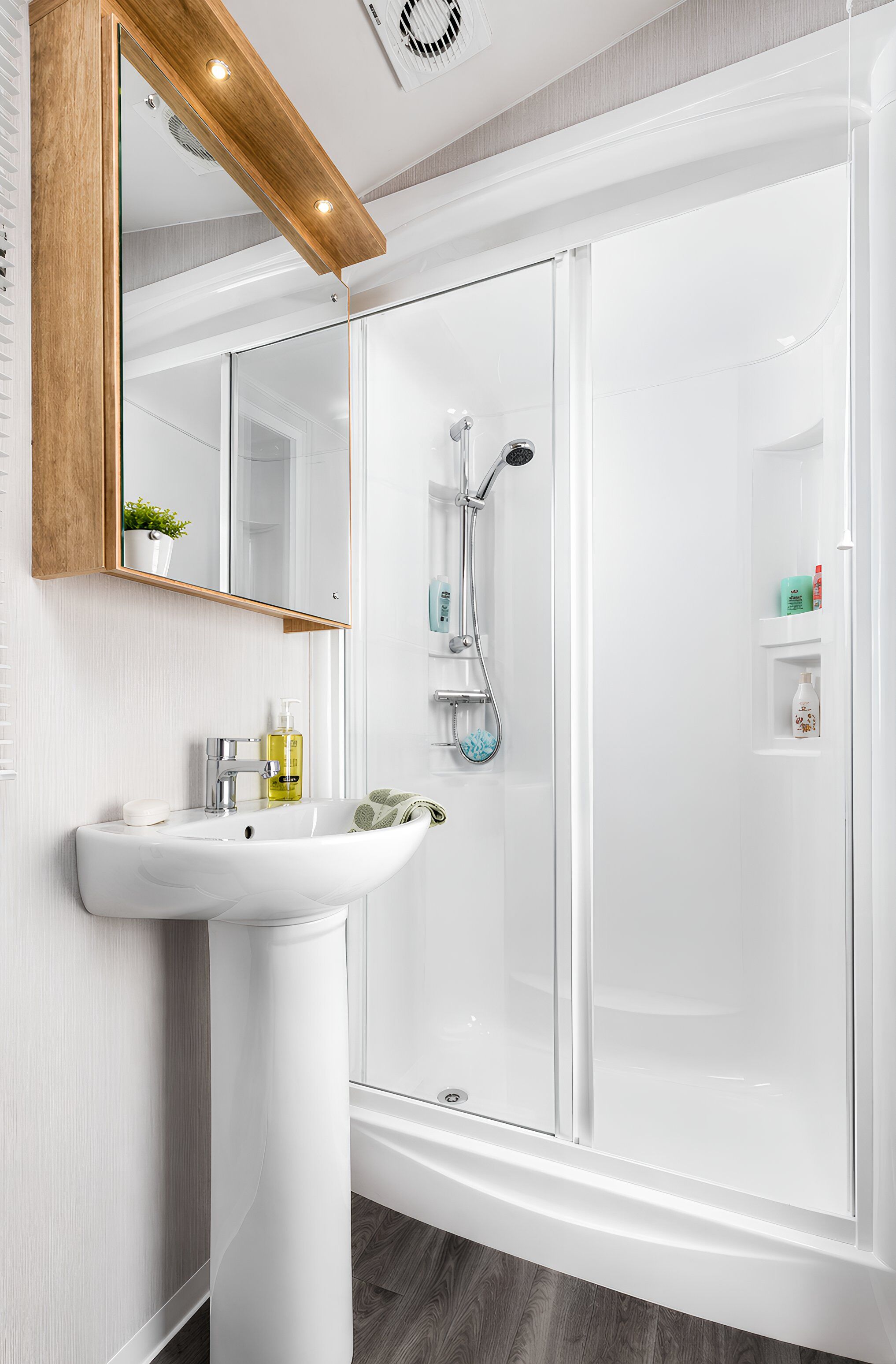 Een moderne badkamer met een wit wastafelmeubel, een douchecabine met glazen wanden en een spiegel met houten lijst.