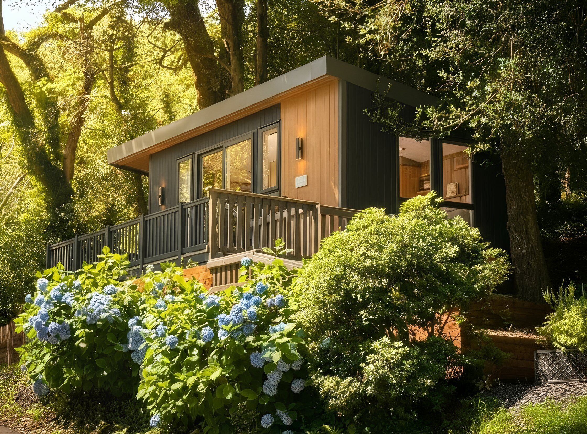 A modern cabin with a wooden deck, surrounded by lush greenery and hydrangea bushes.
