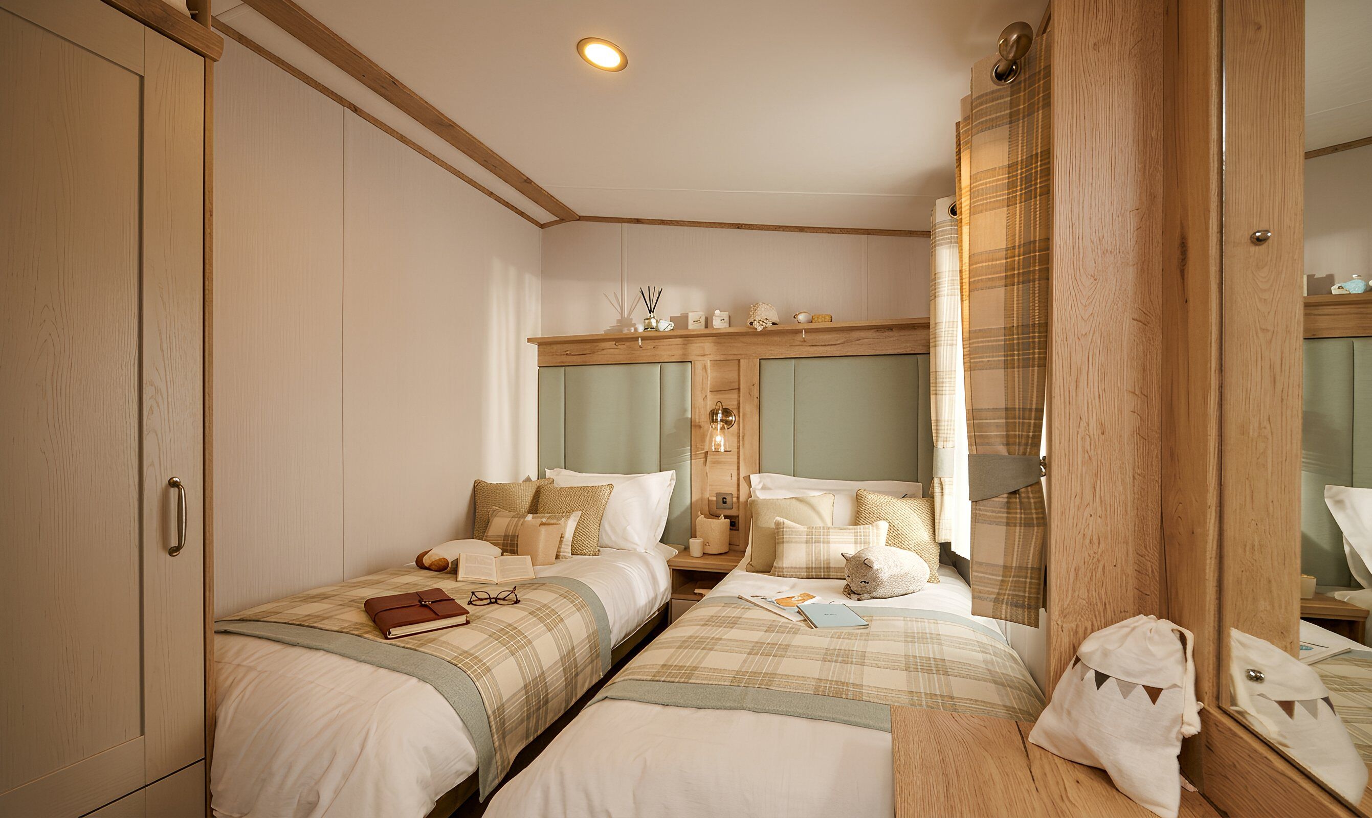 A hotel room with two beds, a wardrobe, a mirror, and a bedside table with a lamp.